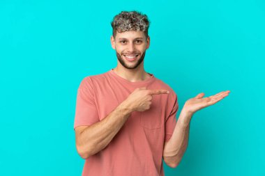 Mavi arka planda izole edilmiş yakışıklı beyaz adam bir ilan vermek için fotokopi makinesini avucunun içinde tutuyor.