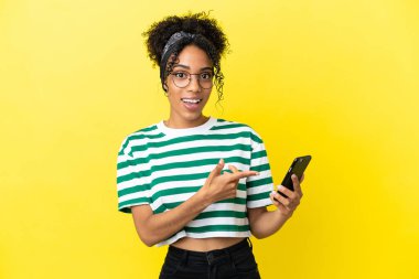 Genç Afrikalı Amerikalı kadın sarı arka planda izole edilmiş ve cep telefonu kullanıyor.