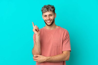 Mavi arka planda izole edilmiş yakışıklı beyaz adam mutlu ve dik duruyor.