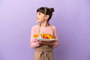 Mor arka planda izole edilmiş waffle tutan küçük beyaz kız.