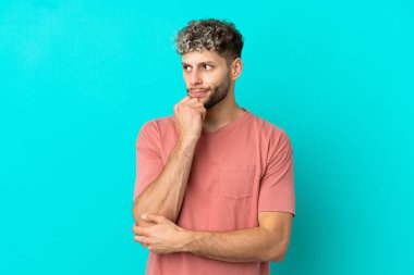 Mavi arka planda soyutlanmış yakışıklı, beyaz bir adam. Şüpheleri ve düşünceleri var.