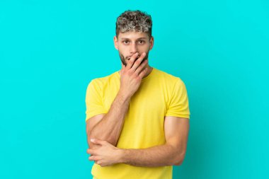 Mavi arka planda izole edilmiş yakışıklı beyaz adam sağa bakarken şaşırdı ve şok oldu.