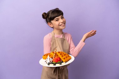 Mor arka planda izole edilmiş waffle 'ları tutan küçük beyaz kız davet etmek için ellerini yana uzatıyor.