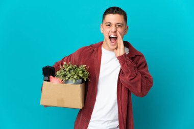 Kafkasyalı genç adam mavi arka planda izole edilmiş bir kutu dolusu şaşırtıcı ve şok edici yüz ifadesiyle hareket ediyor.