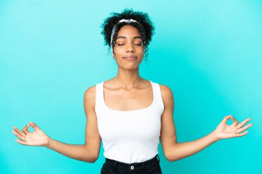 Zen pozunda mavi arka planda izole edilmiş genç Latin kadın.