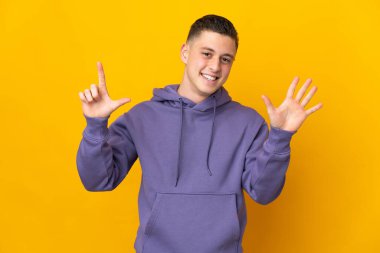 Sarı arka planda izole edilmiş genç beyaz adam parmaklarıyla yediyi saydı.