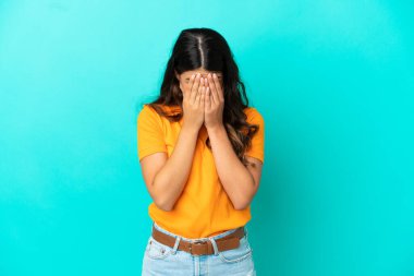 Kafkasyalı genç bir kadın mavi arka planda izole edilmiş, yorgun ve hasta bir ifadeyle.