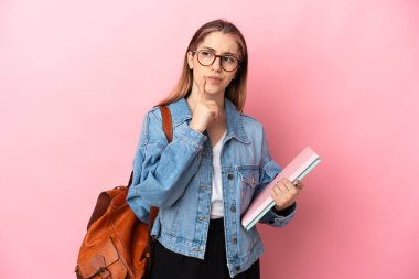 Pembe arka planda izole edilmiş genç beyaz kadın, yukarı bakarken şüphe duyuyor.