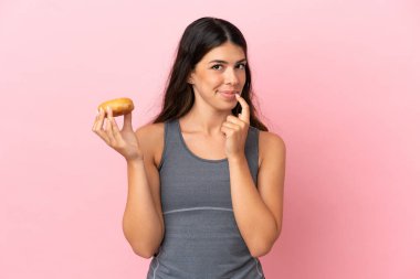 Pembe arka planda izole edilmiş beyaz bir kadın elinde donut tutuyor.