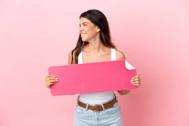 Pembe arka planda izole edilmiş beyaz bir kadın boş bir levha tutuyor ve etrafına bakıyor.