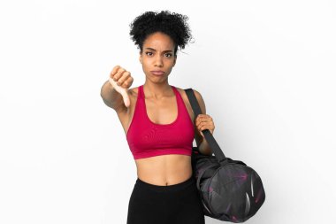 Spor çantalı genç Afro-Amerikan kadın mavi arka planda izole edilmiş, olumsuz ifadeli baş parmağını gösteriyor.
