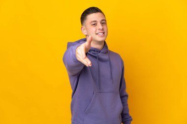 Sarı arka planda izole edilmiş genç beyaz adam iyi bir anlaşma için el sıkışıyor.