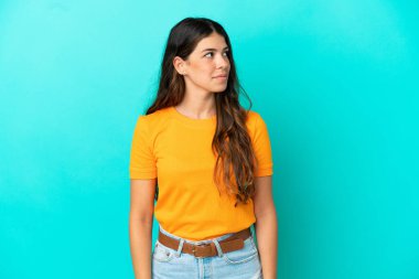Mavi arka planda izole edilmiş genç beyaz kadın yan tarafa bakıyor.