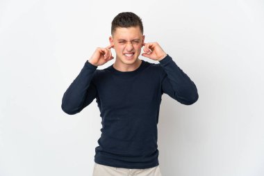 Beyaz arka planda izole edilmiş genç beyaz adam hayal kırıklığına uğramış ve kulaklarını kapatmış.