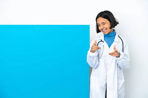 年轻的混合赛女医生 有一张白色背景的大海报 指着前面笑着 — 图库照片