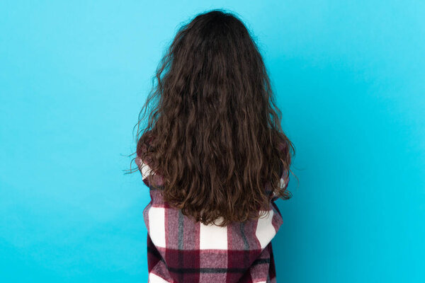 Teenager Russian girl isolated on blue background in back position