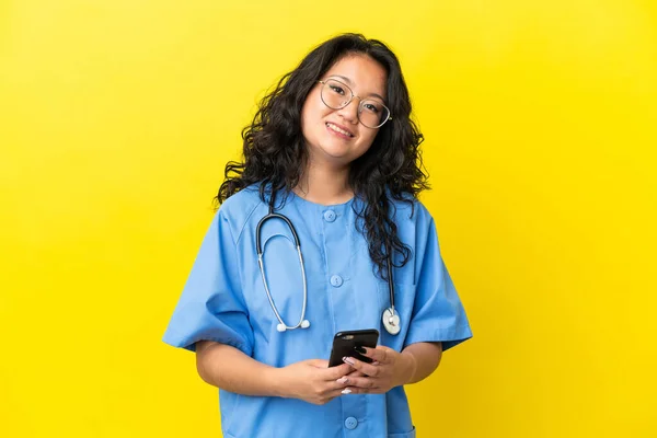 年轻的外科医生 亚洲女人 在黄色背景下被隔离 用手机传送讯息 — 图库照片
