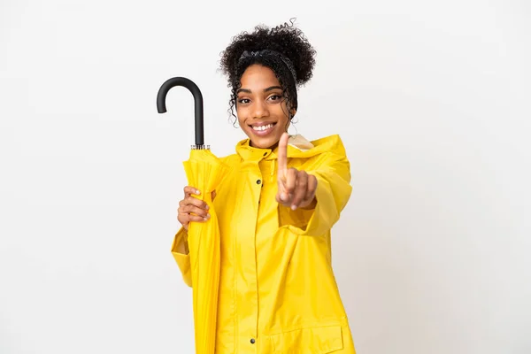 白い背景にレインプルーフコートと傘を身に着けている若い女性は指を見せて持ち上げる — ストック写真