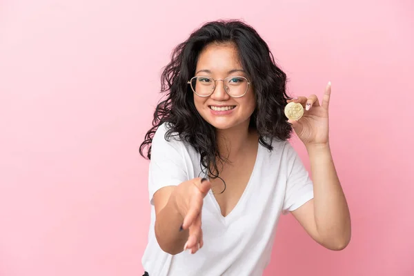 年轻的亚洲女人拿着一枚用粉色背景隔离起来的比特币 握手表示要合上一大笔钱 — 图库照片