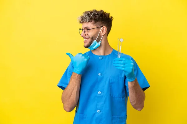 Dentysta Biały Mężczyzna Trzyma Narzędzia Izolowane Żółtym Tle Wskazując Bok — Zdjęcie stockowe