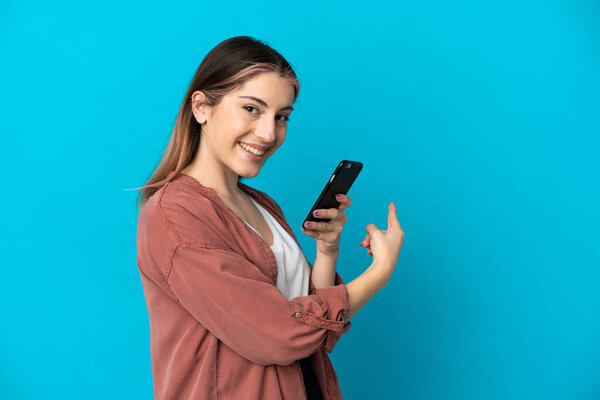 Young caucasian woman isolated on blue background using mobile phone and pointing back