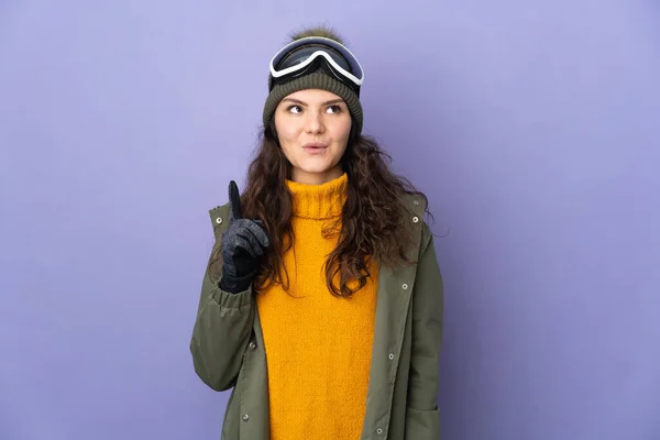 俄罗斯少女 戴着雪板眼镜 与紫色背景隔离 想在举起一只手指头的同时实现这个解决方案 — 图库照片