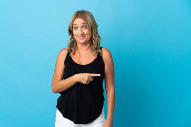 Orta yaşlı, izole edilmiş bir geçmişi olan sarışın bir kadın bir ürünü sunmak için kenarı işaret ediyor.