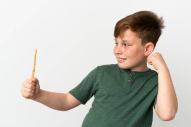 Beyaz arka planda izole edilmiş diş fırçası tutan kızıl saçlı çocuk zaferi kutluyor.