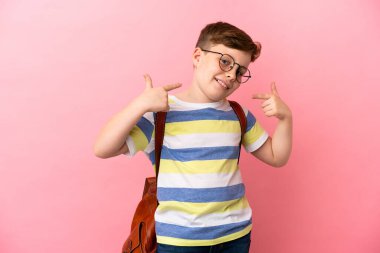 Küçük kızıl saçlı beyaz çocuk pembe arka planda izole edilmiş bir şekilde baş parmak hareketi yapıyor.