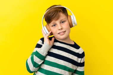 Sarı arka planda izole edilmiş küçük kızıl çocuk müzik dinliyor.