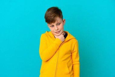 Küçük kızıl saçlı çocuk mavi arka planda izole edilmiş bir şekilde yukarı bakarken bir fikir düşünüyor.