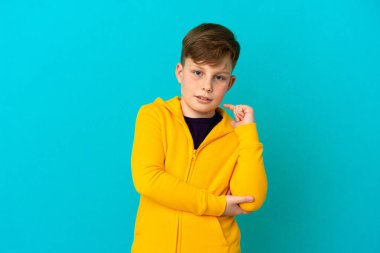 Küçük kızıl saçlı çocuk mavi arka planda yalnız gülüyor.