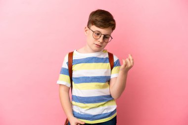 Küçük kızıl saçlı beyaz çocuk pembe arka planda izole edilmiş para hareketi yapıyor.