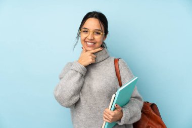 Okula giden melez bir kadın mavi arka planda tek başına gülümsüyor.