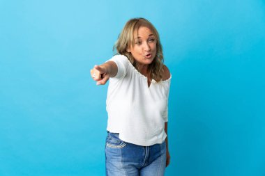 Orta yaşlı sarışın kadın izole edilmiş arka planda hayal kırıklığına uğramış ve ön tarafı işaret ediyor.