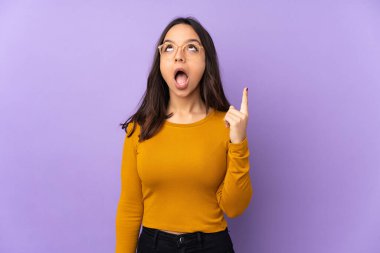 Mor arka planda izole edilmiş genç bir ırk kadını yukarı bakıyor ve şaşırıyor.