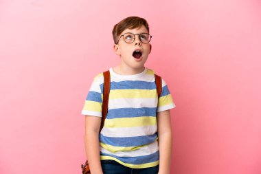 Küçük kızıl saçlı beyaz çocuk pembe arka planda izole edilmiş yukarı bakıyor ve şaşırmış bir ifadeyle