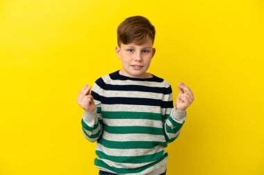 Sarı arka planda izole edilmiş küçük kızıl çocuk para hareketi yapıyor.