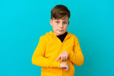 Mavi arka planda izole edilmiş küçük kızıl çocuk geç kalma jesti yapıyor.