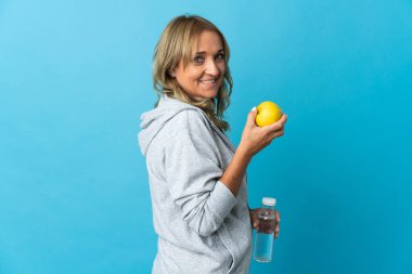 Bir elma ve bir şişe su ile izole edilmiş arka plan üzerinde orta yaşlı sarışın kadın