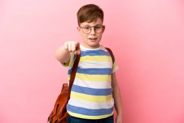 Küçük kızıl saçlı beyaz çocuk pembe arka planda izole edilmiş şaşırmış ve ön tarafı işaret ediyor.