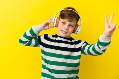Küçük kızıl saçlı çocuk sarı arka planda izole edilmiş müzik dinliyor ve şarkı söylüyor.