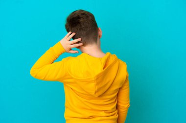 Küçük kızıl saçlı çocuk mavi arka planda izole edilmiş ve düşünüyor.