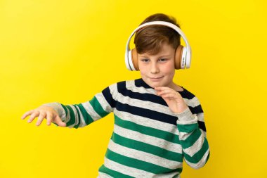 Sarı arka planda izole edilmiş küçük kızıl çocuk müzik ve dans dinliyor.