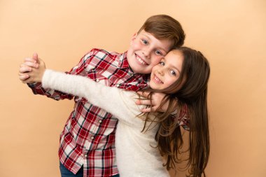 Küçük beyaz erkek ve kız kardeş bej arka planda izole edilmiş.