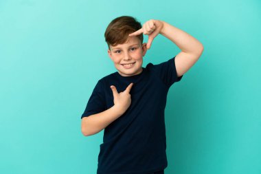 Küçük kızıl saçlı çocuk mavi arka planda izole edilmiş, yüzüne odaklanmış. Çerçeve sembolü