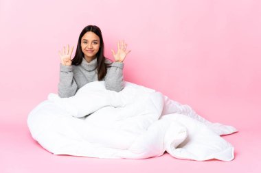 Genç melez kadın pijamasını giymiş yerde oturmuş parmaklarıyla dokuzu sayıyor.