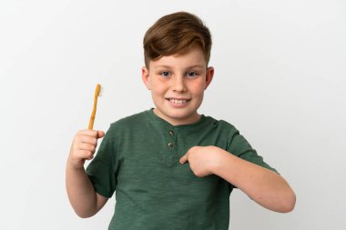 Beyaz arka planda diş fırçası tutan kızıl saçlı çocuk şaşırmış yüz ifadesi ile izole edilmiş.