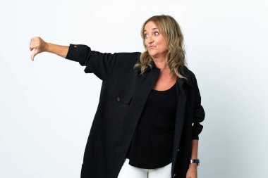 İzole edilmiş beyaz arka planda orta yaşlı sarışın kadın, olumsuz bir ifadeyle baş parmağını gösteriyor.