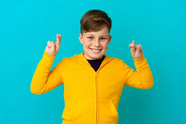 Little Redhead Boy Isolated Blue Background Fingers Crossing Wishing Best — Stock Photo, Image